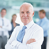Senior healthcare executive with arms crossed and team in background
